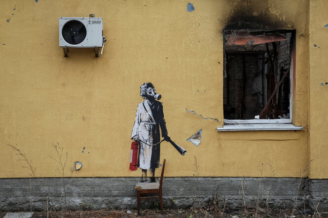 Graffiti von Banksy, eine Frau mit GAsmaske und Feuerlöscher , daneben ein ausgebranntes Fesnter