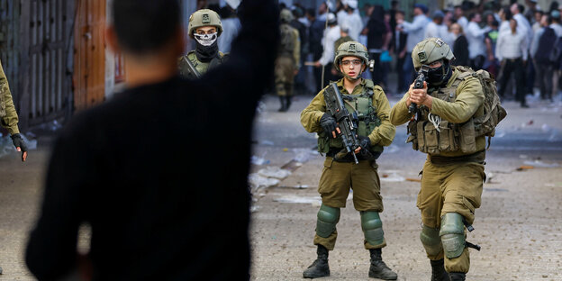 Zwei Soldaten im Hintergrund, im Vordergrund ein gestikulierender Demonstrant