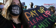 Eine Frau mit Mundschutz hält ein Banner auf dem steht: Pay up, Clean up, Shut up