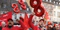 Protestaktion von IG-Metall Mitgliedern in roter Kleidung und gereckten Fäusten Über ihnen schweben rote Ballons in der Form der Zahl Acht