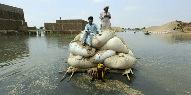 Ein Mann zieht auf einem Floß Säcke mit Korn durch die Flut
