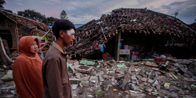 People walk past a destroyed house.
