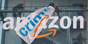 Protestaktion mit einem Plakat an einem Amazon Firmenlogo.