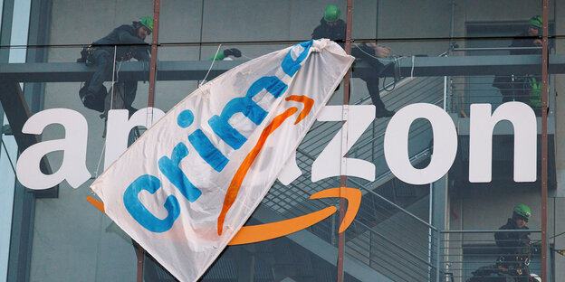 Protestaktion mit einem Plakat an einem Amazon Firmenlogo.