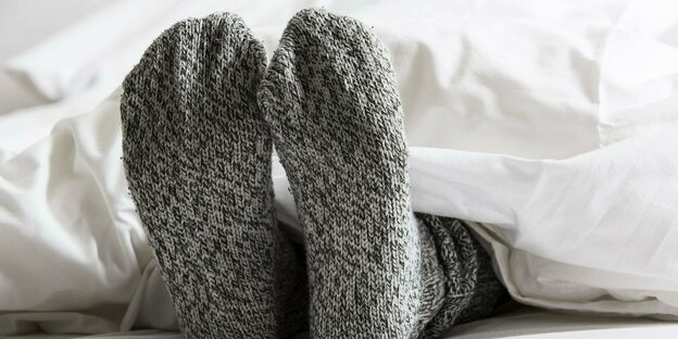Füsse in warmen grauen Socken lugen unter einer Bettdecke hervor