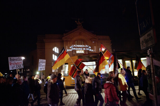 Leuchschrift auf einem Gebäude, davor ein Demonstrationszug