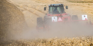 Eine Traktor fährt auf einem Kornfeld und ist von Staub umgeben