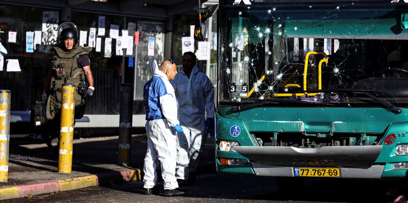 Polizisten untersuchen den bei Explosionen zerstörten Bus.