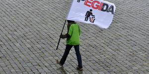 Mann mit Pegida-Fahne läuft über leeren Platz