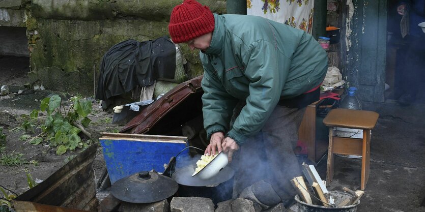 Auf einem Behelfsherd in Trümmern eines Hauses in Lyman, Region Donezk, kocht eine Frau Kartoffeln