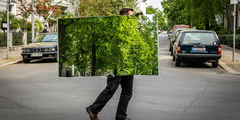 Ein Mann trägt ein Bild mit einem Baum über eine Straße.