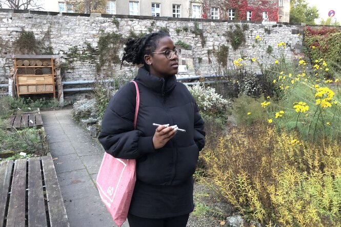 Eine Frau steht in einem Garten , in ihrere Hand hält sie ein Handy