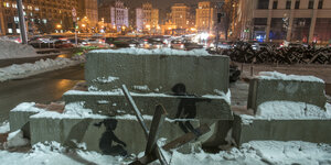 2 Kinderfiguren auf einer Wippe, Panzersperren im schnee, nächtliche Kulisse von Kiews Unabhängigkeitsplatz