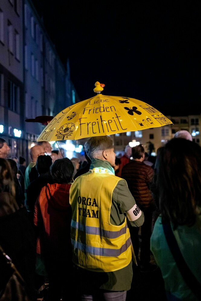 Ein Mann mit gelbem Regenschirm und in Warnweste auf der "Orga Team" geschrieben steht