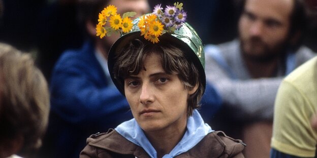 Petra Kelly trägt einen Militärhelm, der mit Blumen geschmückt ist