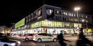 Das Karstadt Gebäude am Hermannplatz bei Nacht mit Autos die davor vorbeifahren