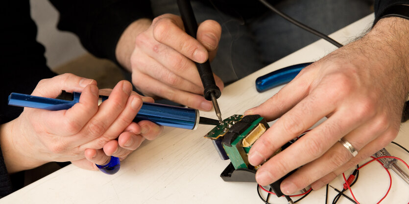 Reparatur im Repair-Cafe in Berlin im Bezirk Kreuzberg: Zwei Menschen schrauben am Netzteil eines 20 Jahre alten CD-Spielers