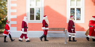 "Weihnachtsmänner" und eine "Weihnachtsfrau" gehen im Rahmen einer Weihnachtsmannschulung vor einem Gebäude entlang.