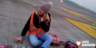 Standbild aus einem Livestream: Eine Aktivistin sitzt mit festgeklebter Hand auf dem Rollfeld