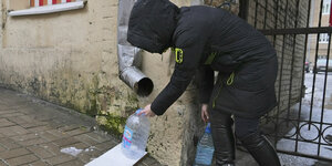 Eine Ukrainerin fängt Regenwasser unter einem Fallrohr mit einer Plastikflasche auf