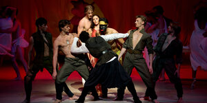 Eine Aufnahme aus Neumeiers Othello-Inszenierung von 2013 zeigt eine Gruppe von Tänzern um die Hauptfiguren Othello und Desdemona, darunter ein Tänzer mit schwarz bemaltem Gesicht.