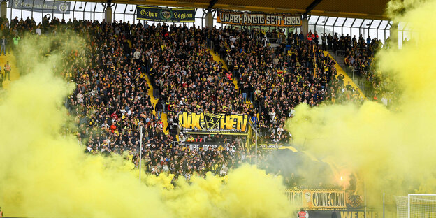 Fans im Stadion in gelbem Rauch.
