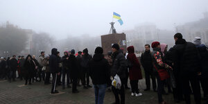 Menschen versammeln sich im Nebel vor dem zentralen Platz in Kherson, auf einer Statue weht eine kleine ukrainische Flagge