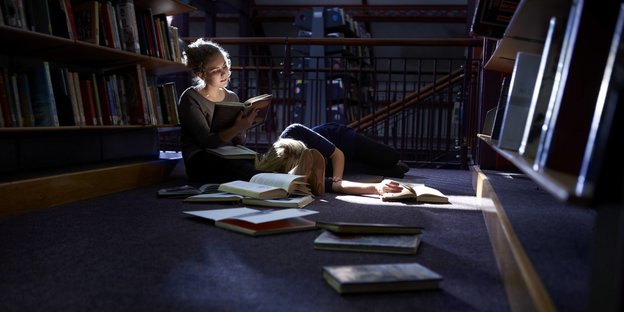 Studentinnen lernen in der Bibliothek. Eine ließt, die andere schläft.