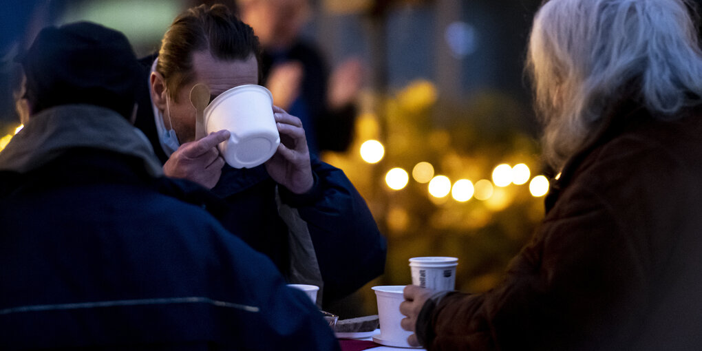 Drei Männer nehmen eine warme Mahlzeit des Caritas-Foodtruck in Charlottenburg-Wilmersdorf ein.