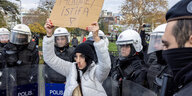 Eine Demonstrantin hebt umringt von Polizisten ein Schild in die Höhe