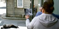 Personen stehen an einer Straßenecke und betrachten ein Schwarz-Weiß-Foto desselben Ortes zum Vergleich.
