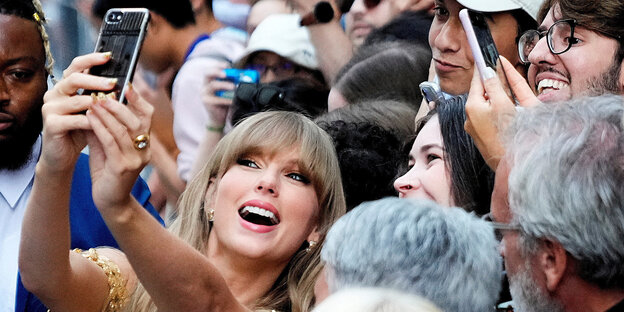 Taylor Swift steht in einer Gruppe von Fans und macht ein Selfie