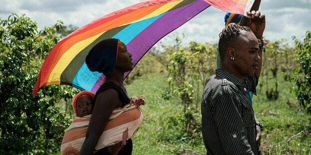 A man with a rainbow flag and a woman with a child are walking