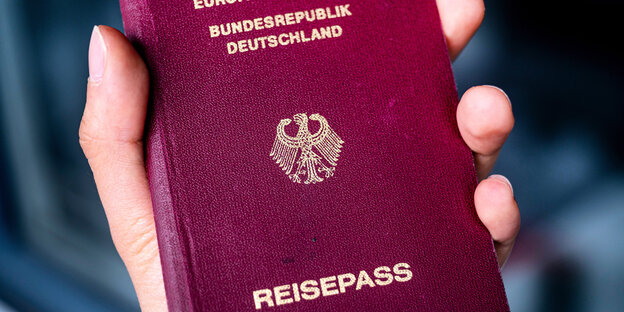 A hand holds the red German passport
