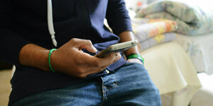 Junge in Unterkunft für minderjährige unbegleitete Geflüchtete schaut auf sein Handy