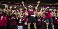 Männliche Fans jubeln in Katar-Shirts im Stadion