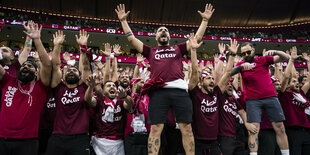 Männliche Fans jubeln in Katar-Shirts im Stadion