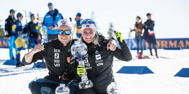 Mann und Frau knien im Schnee mit Siegerpokalen vor sich