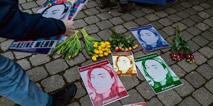 Eine Person legt Blumen und bunte Flugblätter mit einem Foto von Besma A. auf ein Kopfsteinpflaster.