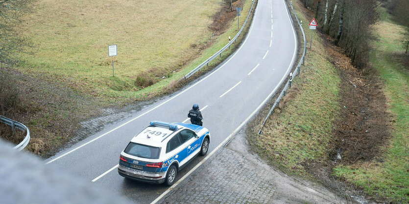 Ein Polizist vor einem Polizeiwagen auf einer Landstraße