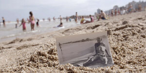 Schwarz-Weiß-Foto einer jungen Frau mit Baby im Sand eines Strandes am Meer