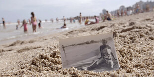 Schwarz-Weiß-Foto einer jungen Frau mit Baby im Sand eines Strandes am Meer