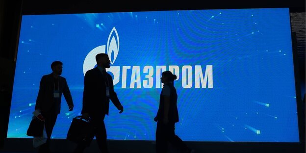 Silhouetten von Menschen vor einem großen Bildschirm, auf dem das Gazprom-Logo zu sehen ist