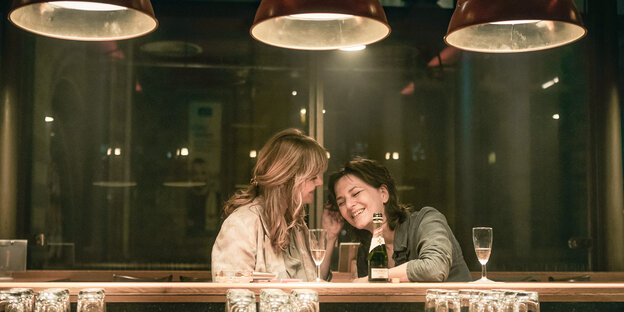 Zwei Frauen einander zugeneigt, Sekt trinkend an einer Bar