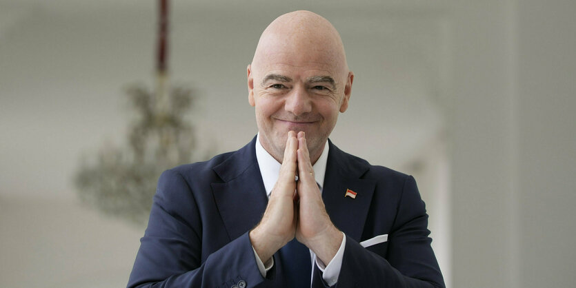 Gianni Infantino faltet die Hände wie zum Gebet und grinst dämlich