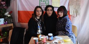 Drei dunklehaarige Frauzen vor einer Iran-Flagge in einem Zelt