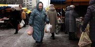 Eine Frau, in einen dicken Wintermantel gekleidet, geht mit Einkaufstüten an Marktständen entlang