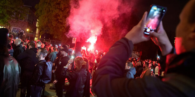 Jemand fotografiert im Hamburger Schanzenviertel mit dem Smartphone eine Menschenmenge, in der Pyrotechnik abgefackelt wird.
