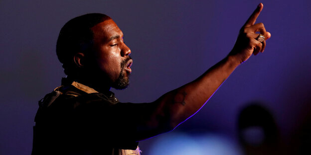 Kanye West, seitlich fotografiert, streckt den Arm aus und hebt den Finger