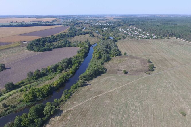 Zwischen zwei Felder an einem kleinen Fluss mit Bäumen am Ufer liegt ein drittes Feld